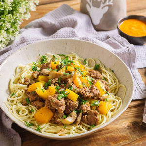 Яичная лапша с грибами и домашним фаршем | Deep plate with spaghetti, minced meat, chopped parsley, yellow bell pepper. Nearby is a bowl with sauce, a fork and a knife, a table napkin, a kitchen waffle towel. Serving per person.