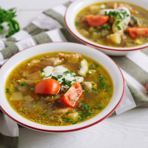 суп с курицей,чечевицей и сметаной | Two plates of chicken soup with vegetables, lentils and sour cream. Large slices of tomato and chopped parsley. On a white wooden table and a kitchen towel.